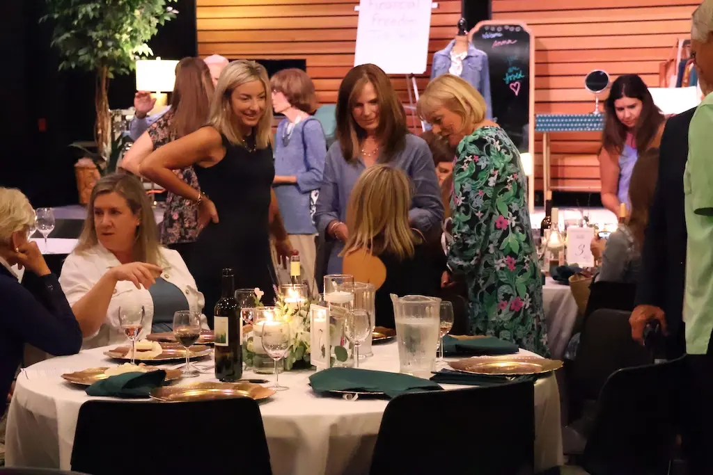 Guests mingling and chatting around decorated dinner tables during a lively community fundraising event