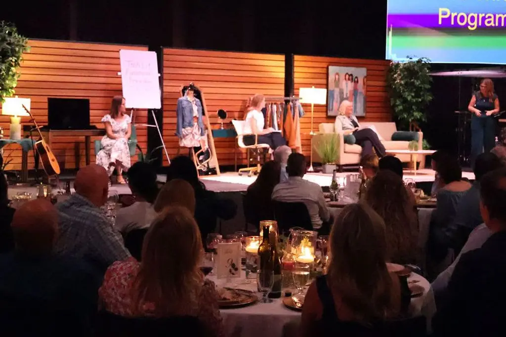 Guests seated at tables watching a live panel discussion and presentation on stage during a community fundraising dinner event